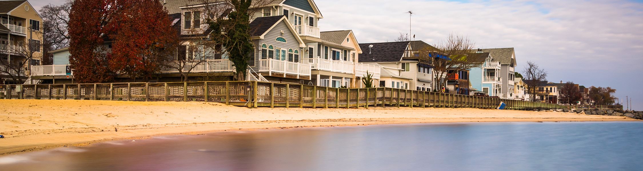 Houses lining a beach with a wooden fence surrounding the houses. 